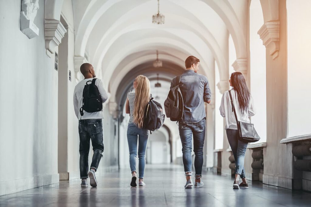 four students with backpacks walk down the hall of a college campus