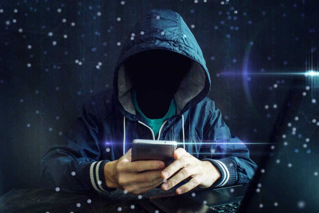hooded hacker uses phone for COVID-19 scams