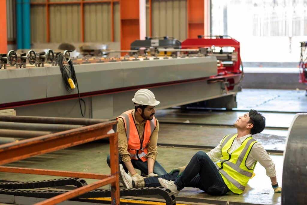 A worker helping another worker after a workplace injury by giving him first-aid.