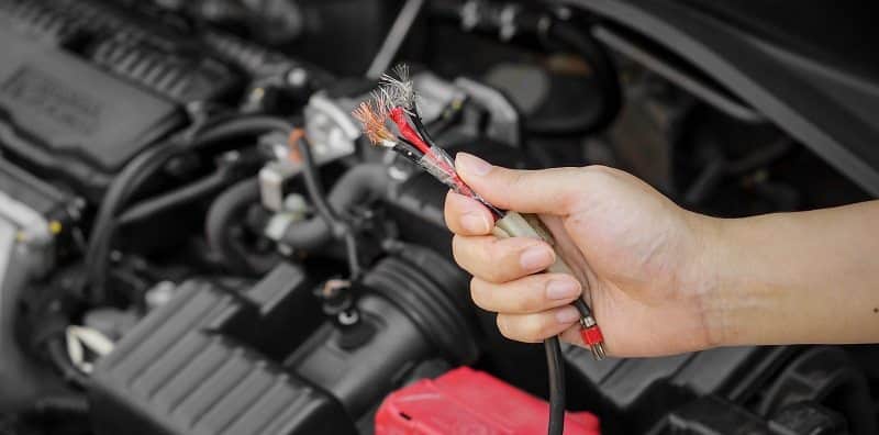 Man holding frayed wire next to car engine